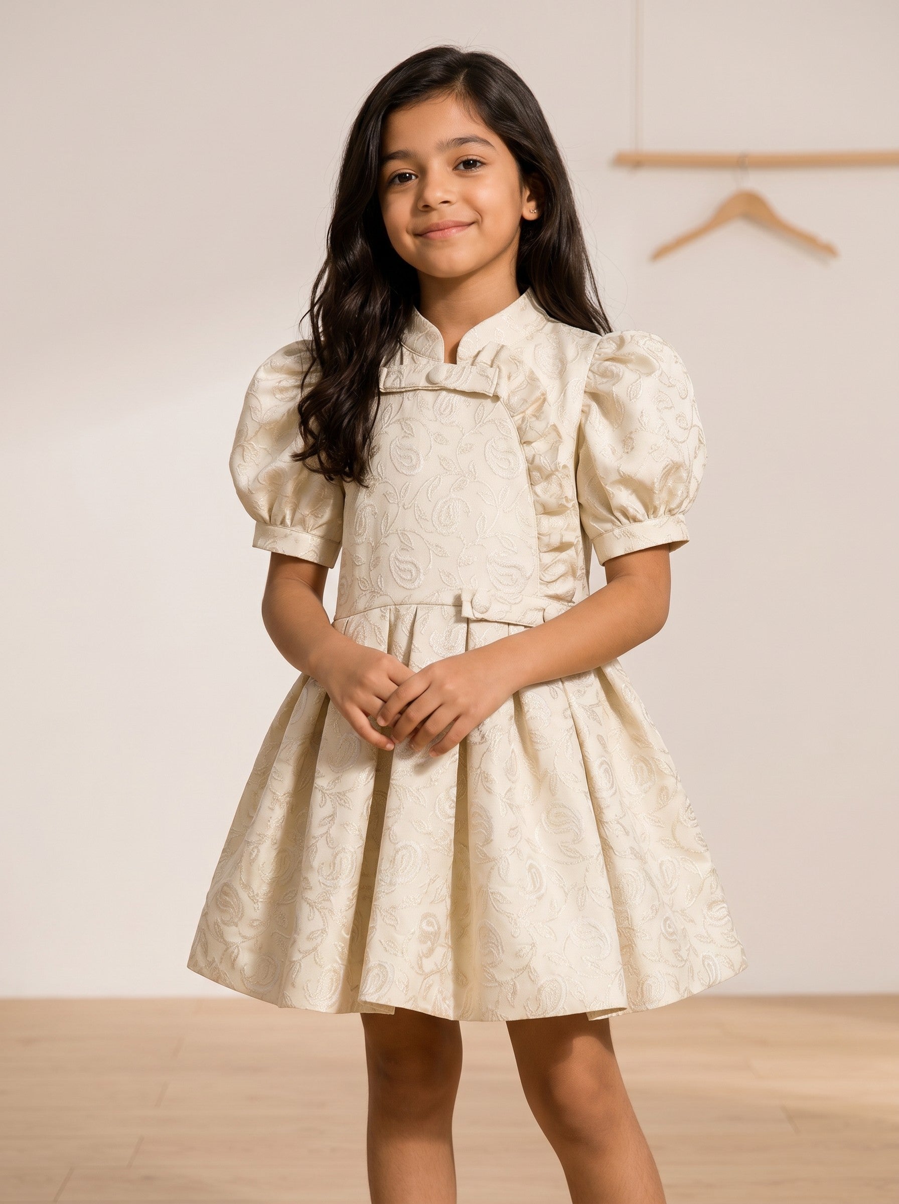 Girl wearing a Baby Kids Cloths cream jacquard dress with puff sleeves, floral pattern, and ruffle side-button detail.