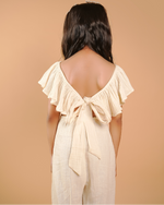 girl wearing a beige jumpsuit with ruffled sleeves against a beige background