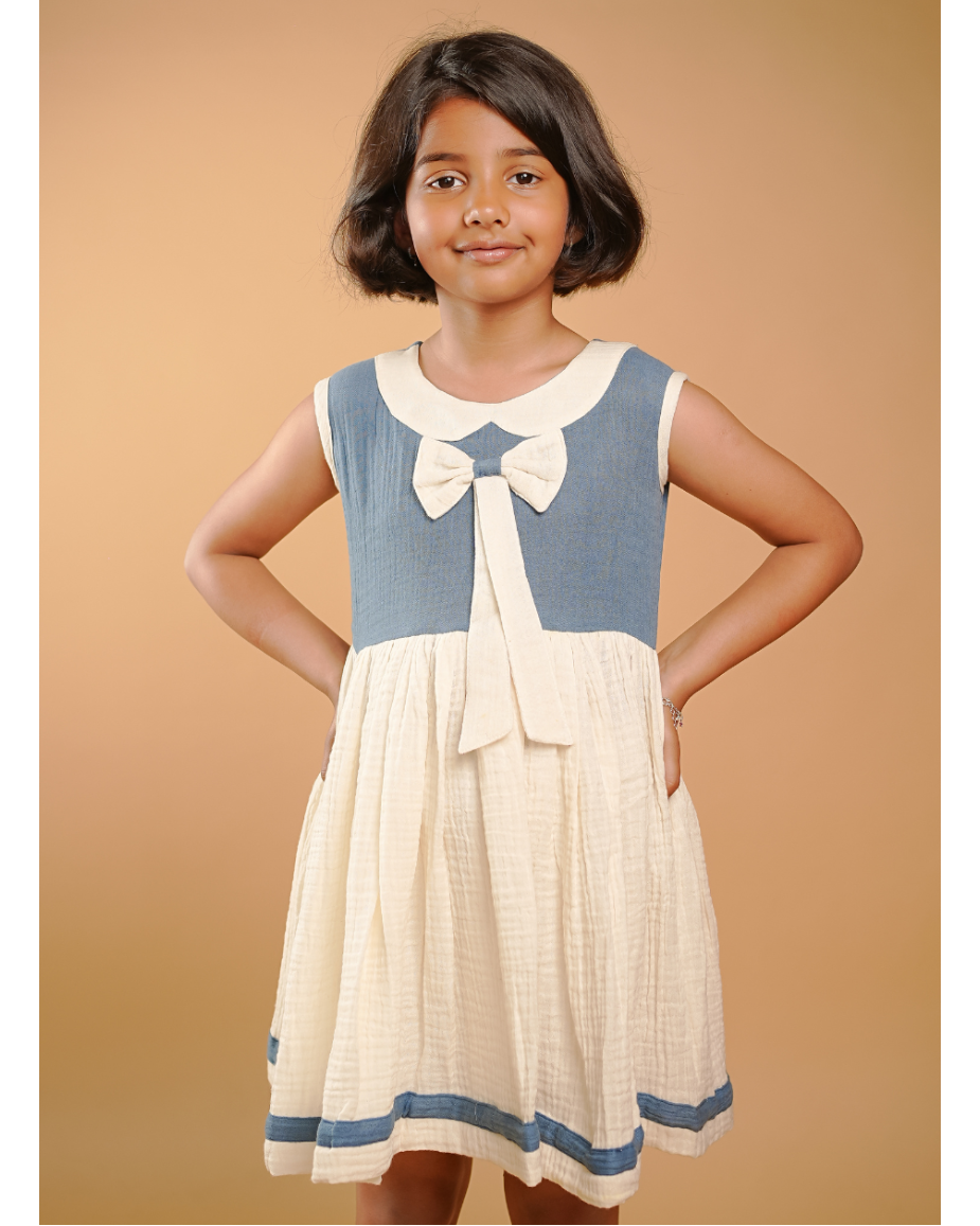 Young girl wearing a blue and white dress with a bow tie collar against a beige background