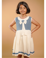 Young girl wearing a blue and white dress with a bow tie collar against a beige background