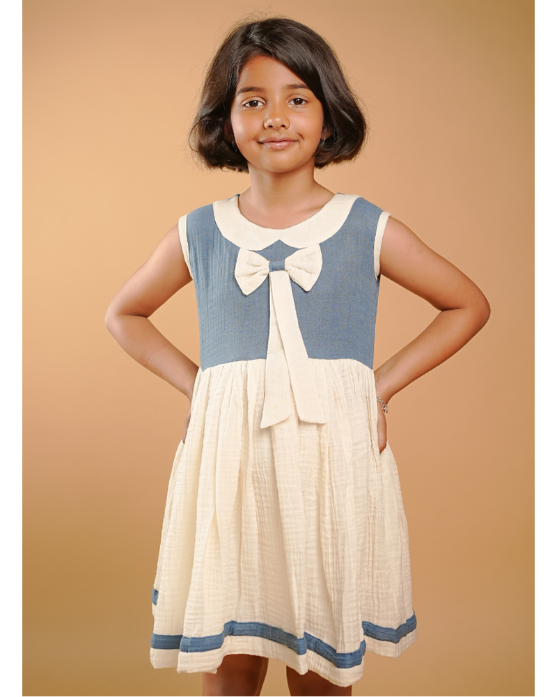 Young girl wearing a blue and white dress with a bow tie collar against a beige background