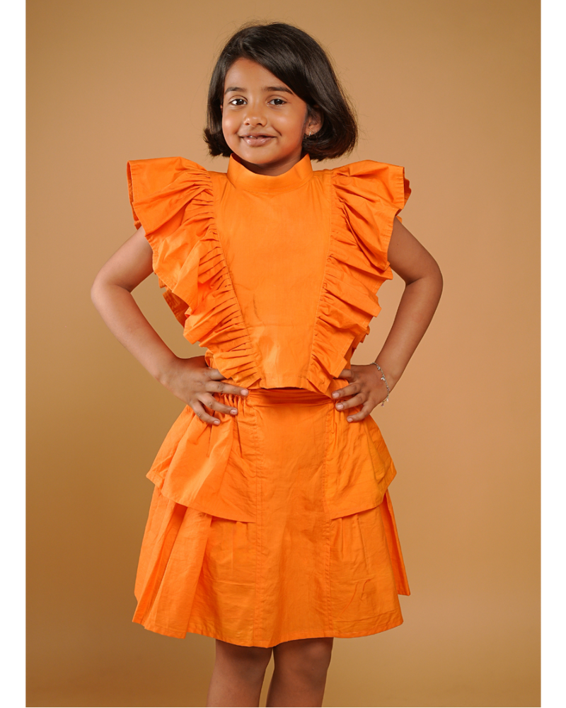 Young girl wearing an orange dress with ruffled details against a beige background