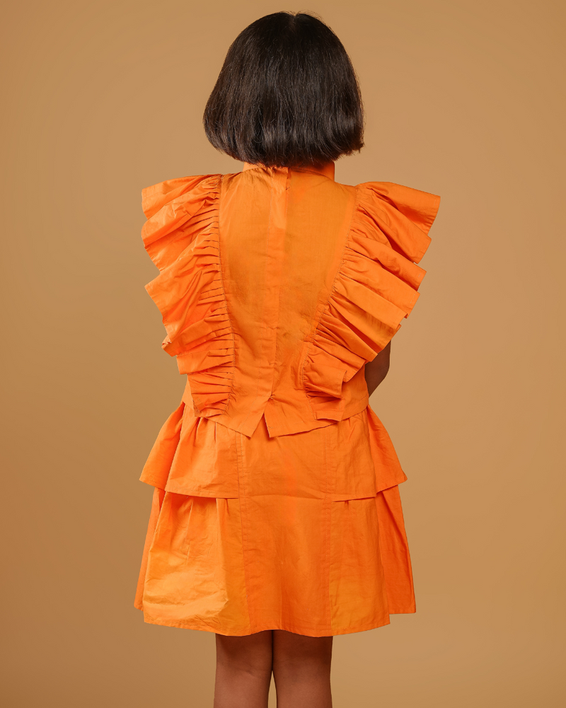 Person wearing an orange dress with ruffled details on a brown background