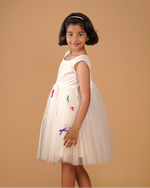 Young girl wearing a white dress with colorful designs on a beige background