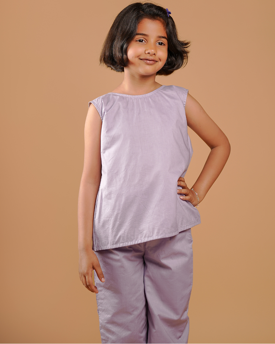 Young girl wearing a light purple sleeveless top and pants against a beige background