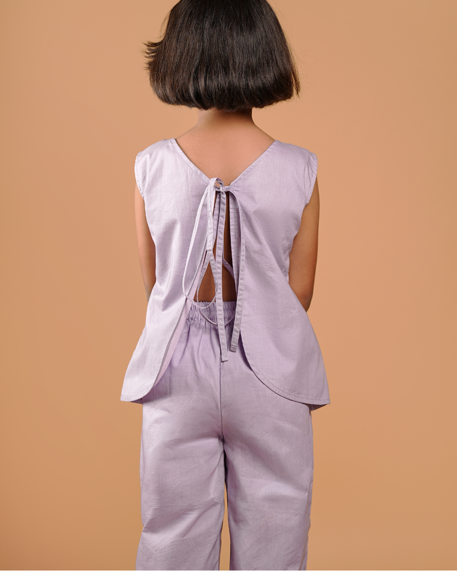 Person wearing a light purple sleeveless top and pants against a beige background