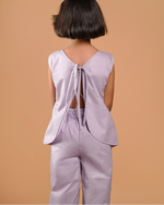 Person wearing a light purple sleeveless top and pants against a beige background