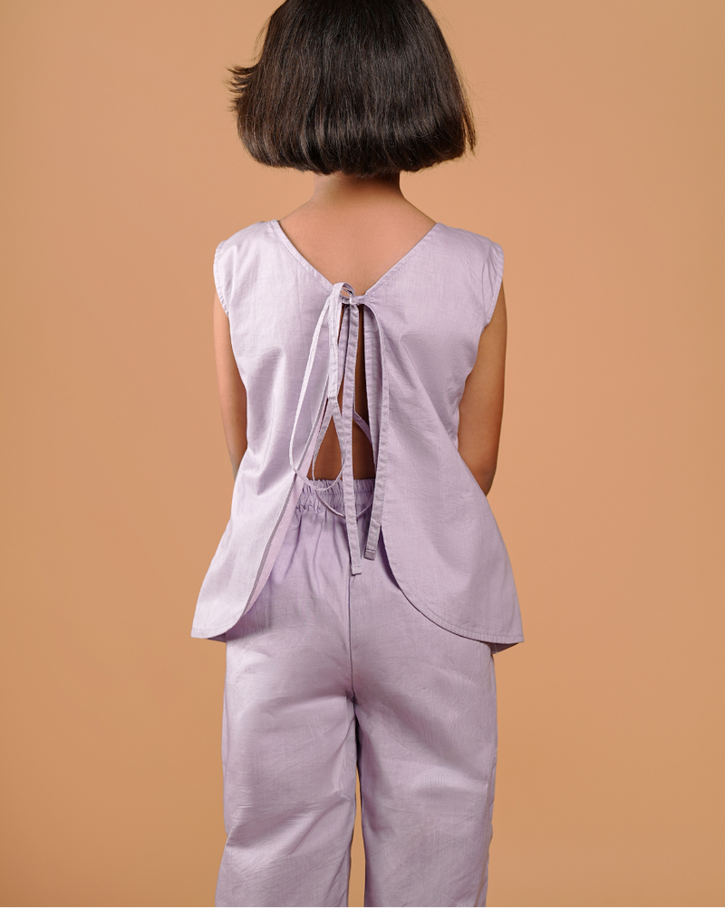Person wearing a light purple sleeveless top and pants against a beige background