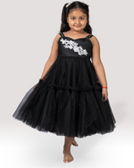 Young girl wearing a black dress with white floral embroidery on a white background