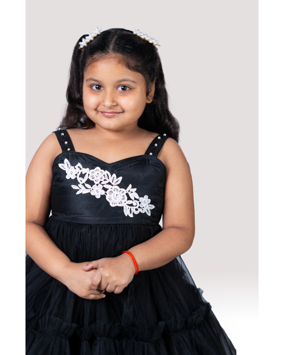 Young girl wearing a black dress with white floral embroidery on a plain background