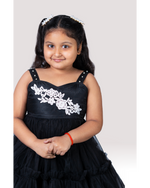 Young girl wearing a black dress with white floral embroidery on a plain background