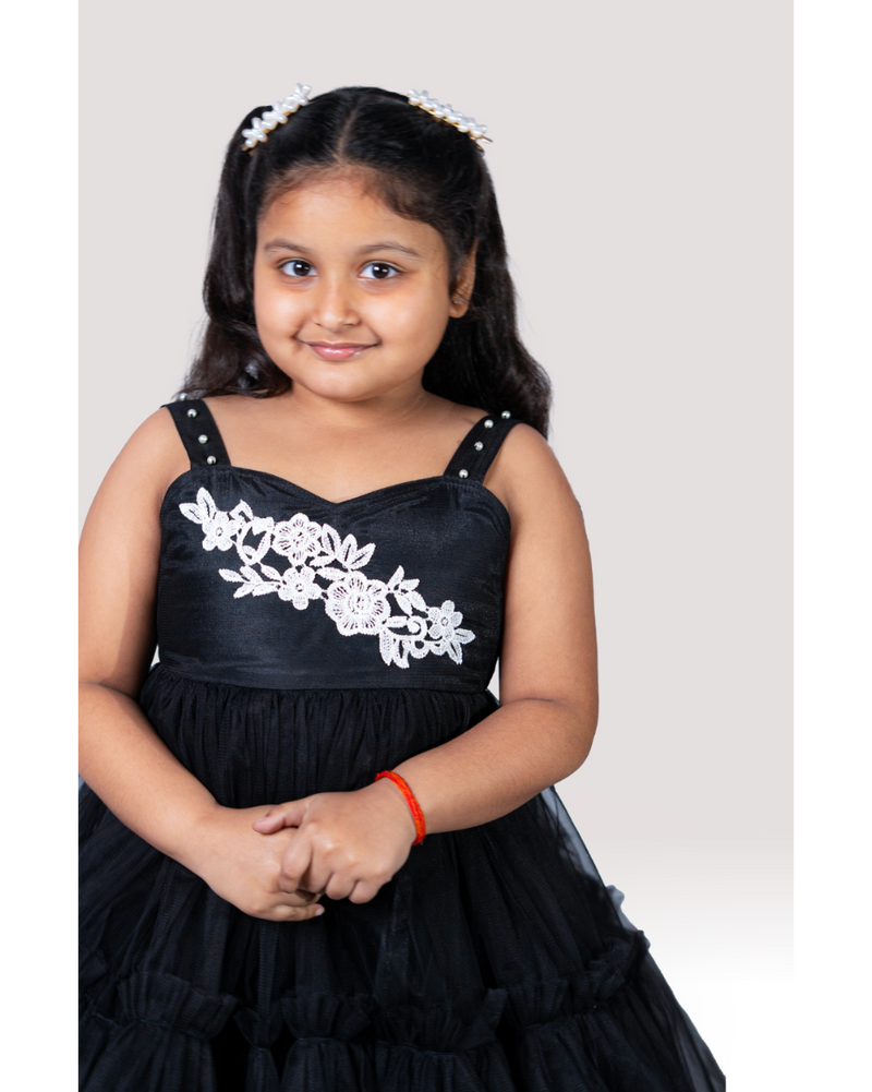 Young girl wearing a black dress with white floral embroidery on a plain background