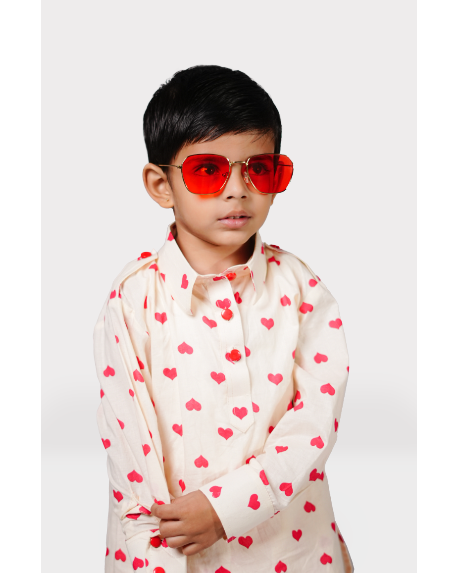 Child wearing a cream shirt with red heart patterns and red sunglasses on a white background