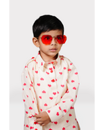Child wearing a cream shirt with red heart patterns and red sunglasses on a white background