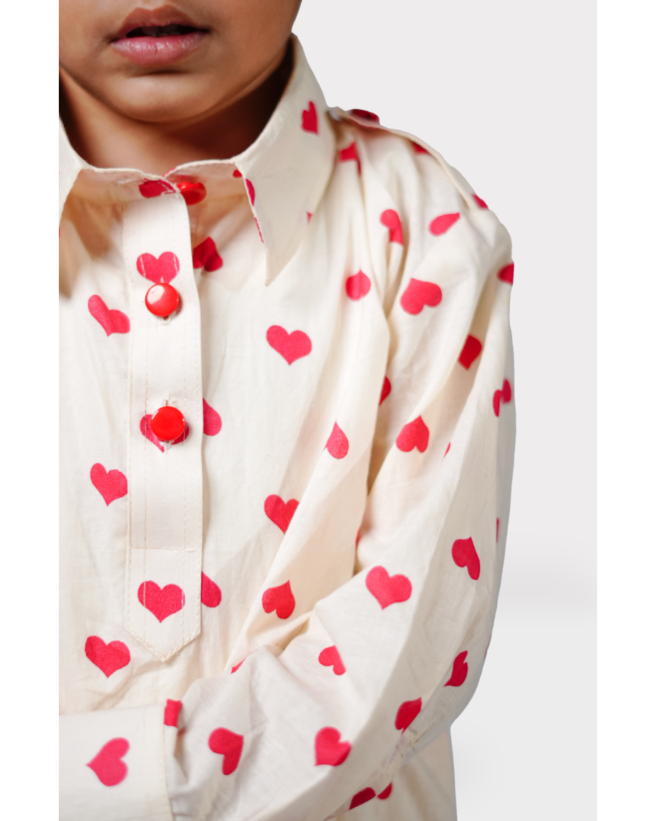 Close-up of a child wearing a cream shirt with red heart patterns on a white background