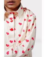 Close-up of a child wearing a cream shirt with red heart patterns on a white background