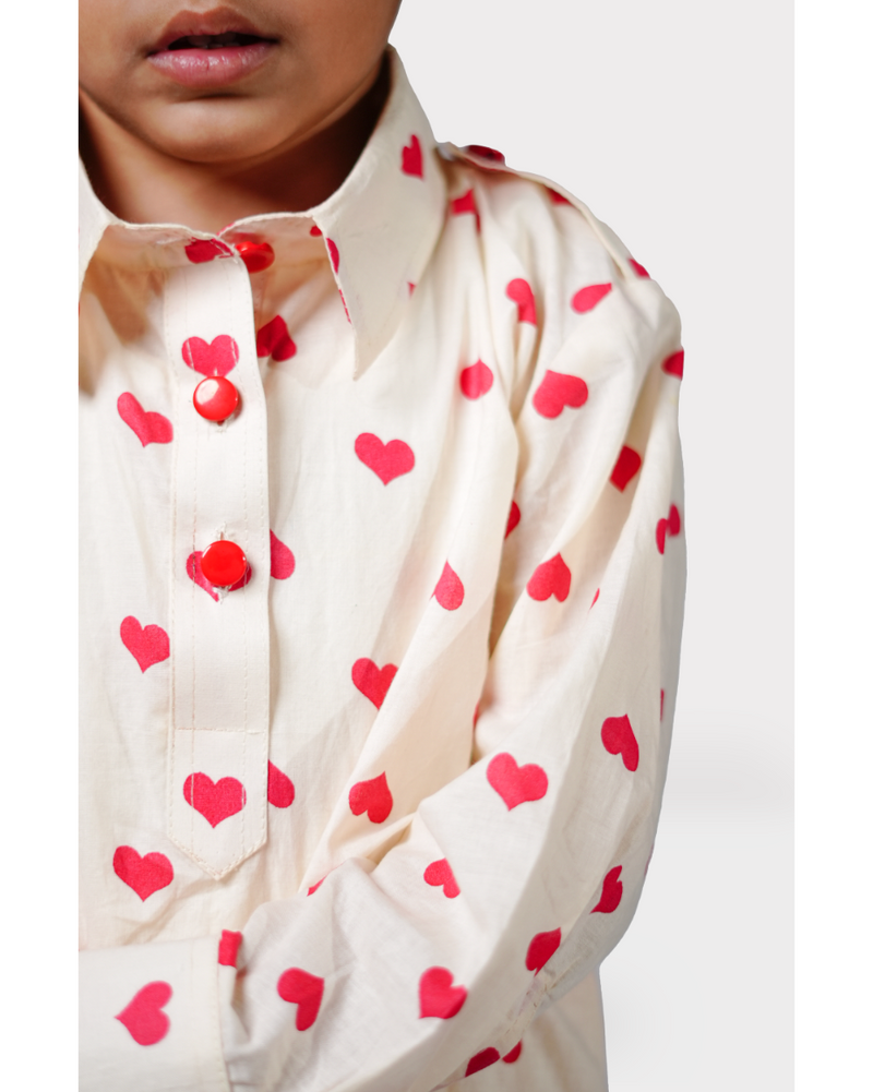 Close-up of a child wearing a cream shirt with red heart patterns on a white background