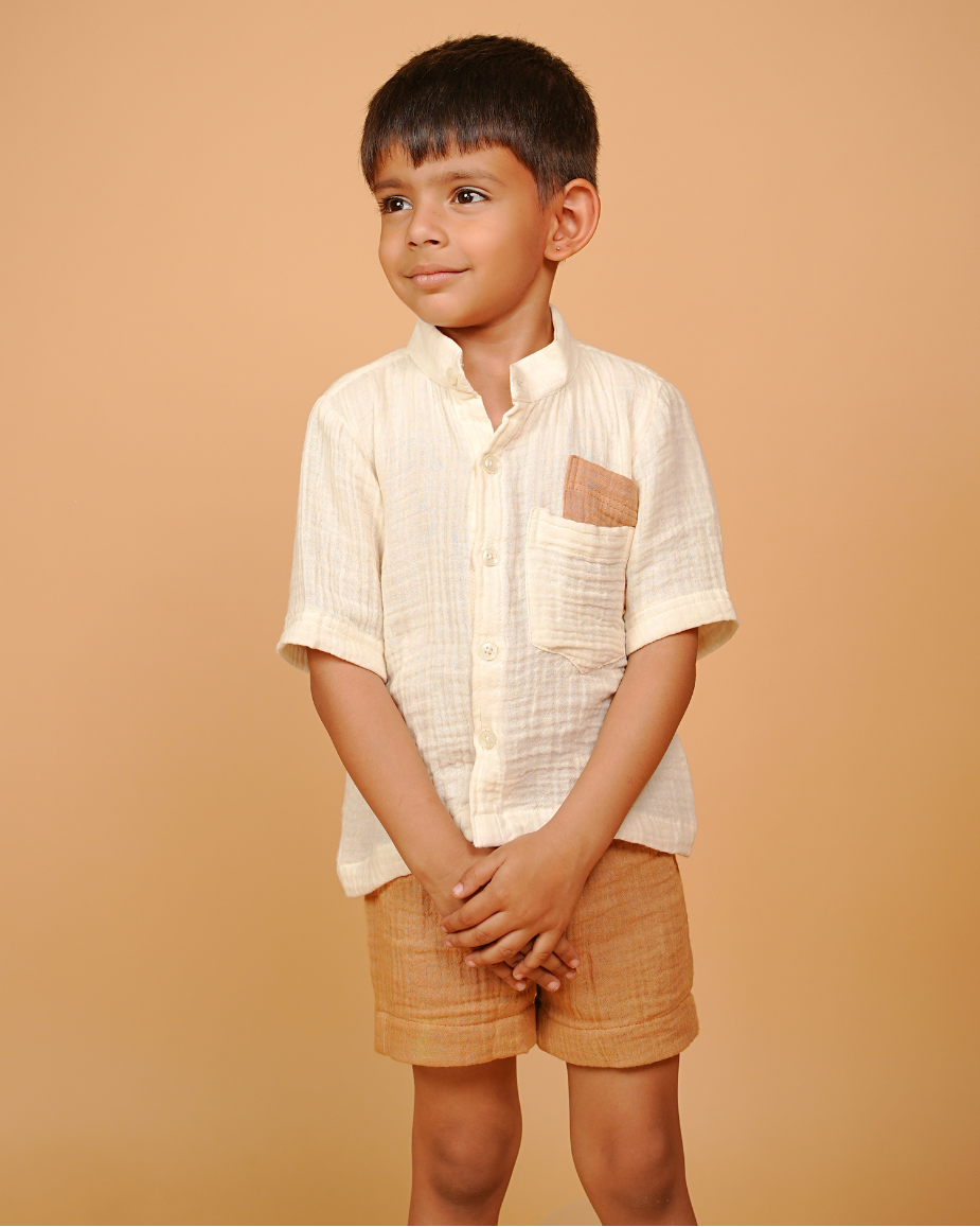 Young boy wearing a white shirt and beige shorts against a beige background