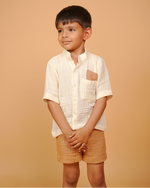 Young boy wearing a white shirt and beige shorts against a beige background