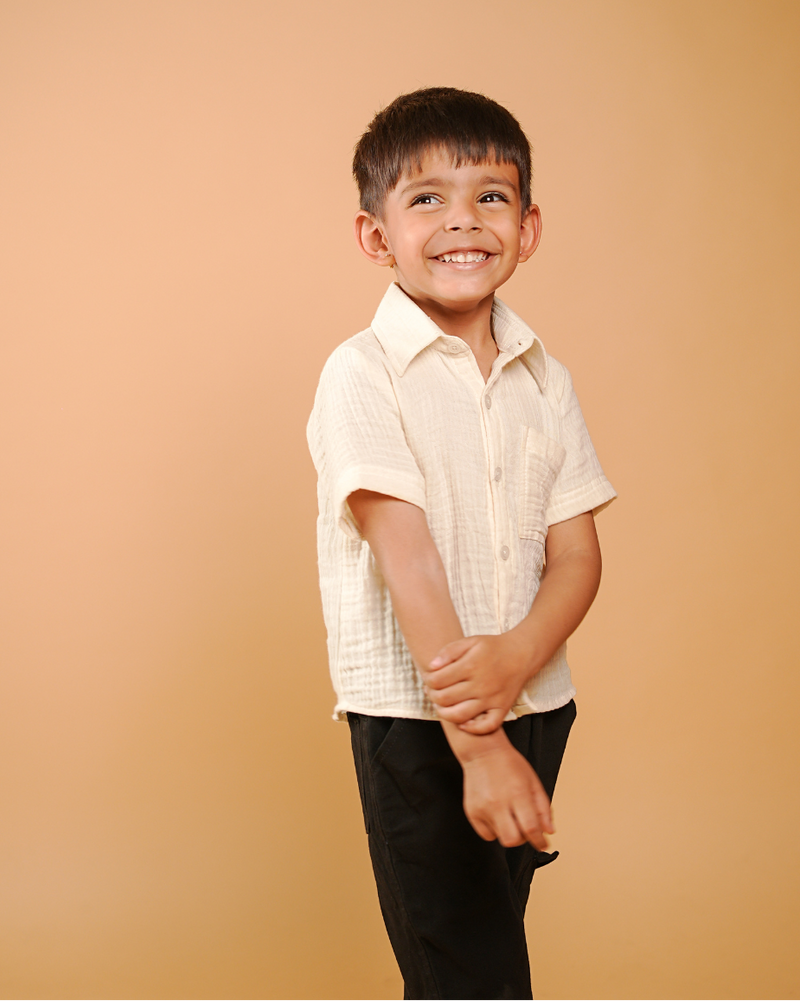 Child wearing a white shirt and black pants against a beige background