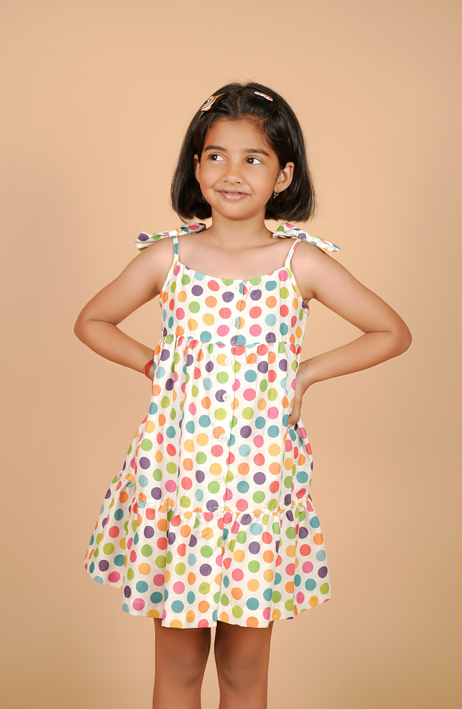 Young girl wearing a colorful polka dot dress against a beige background