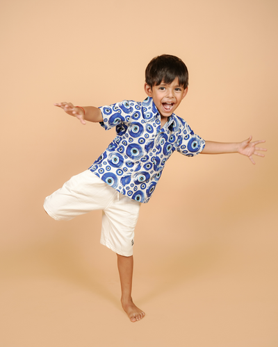 Child wearing a blue patterned shirt and white shorts on a beige background