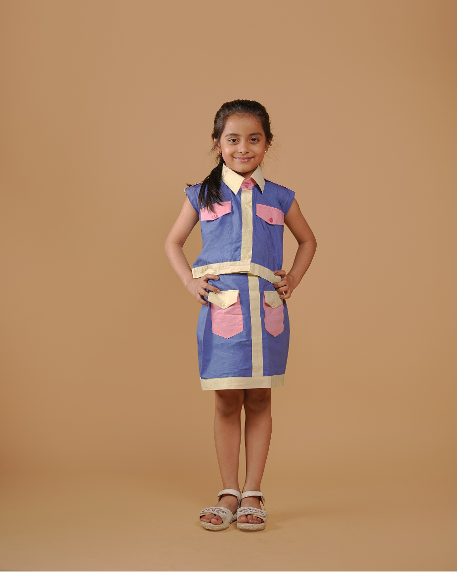 Young girl wearing a blue and pink dress with a vest on a beige background