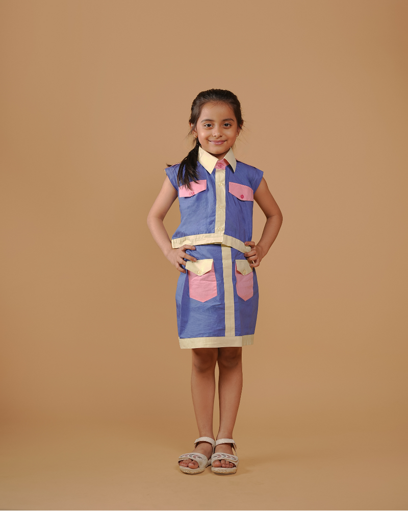 Young girl wearing a blue and pink dress with a vest on a beige background