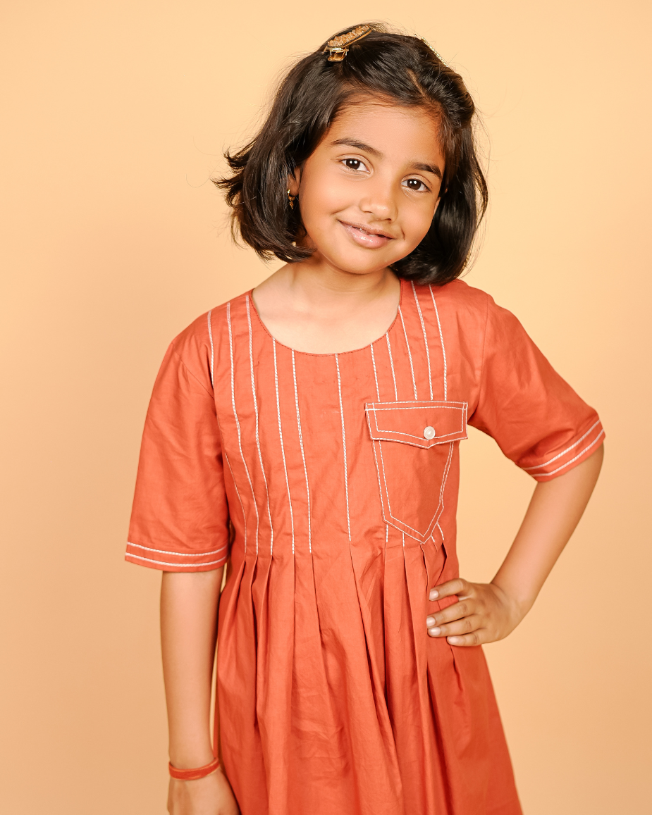 Young girl wearing an orange dress with white stripes on a beige background