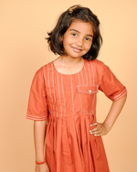 Young girl wearing an orange dress with white stripes on a beige background