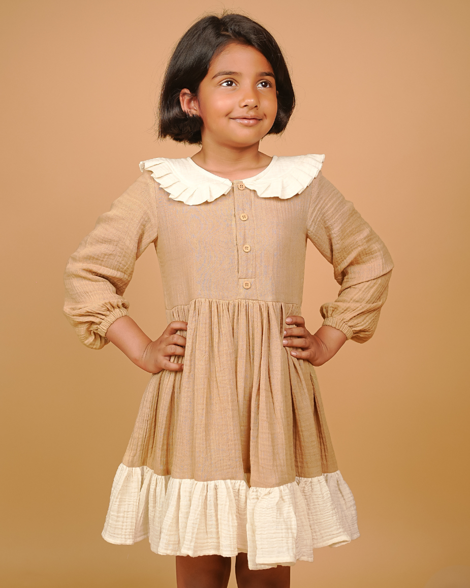 Young girl wearing a beige dress with a white collar against a beige background