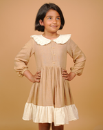 Young girl wearing a beige dress with a white collar against a beige background