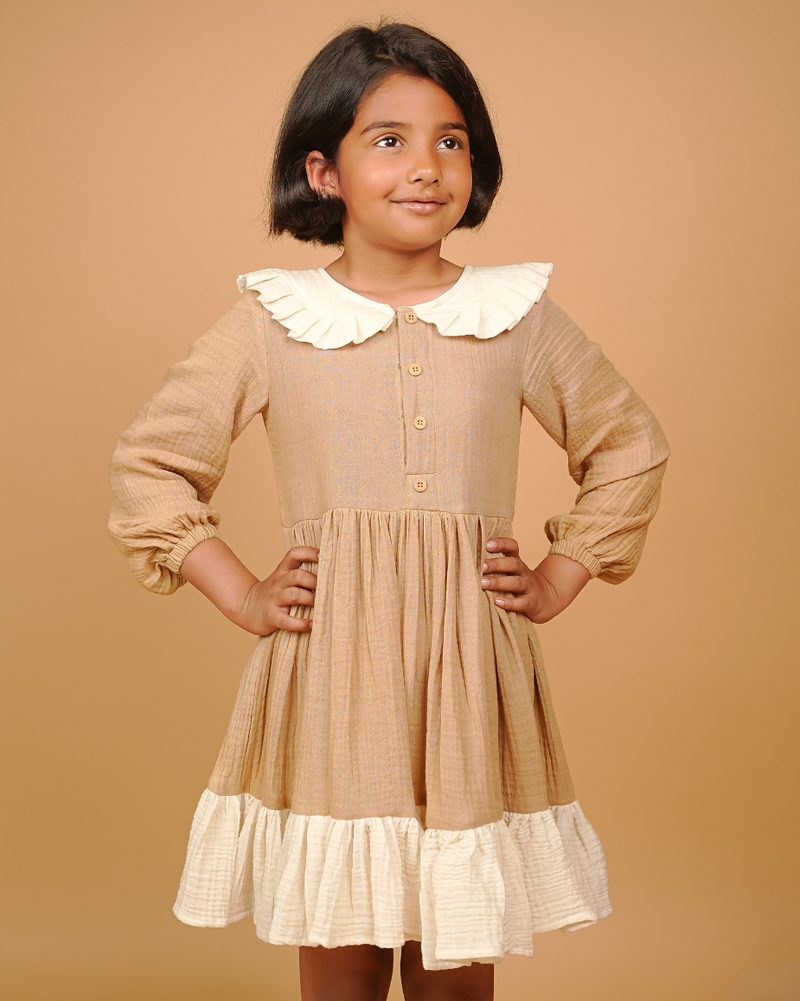 Young girl wearing a beige dress with a white collar against a beige background