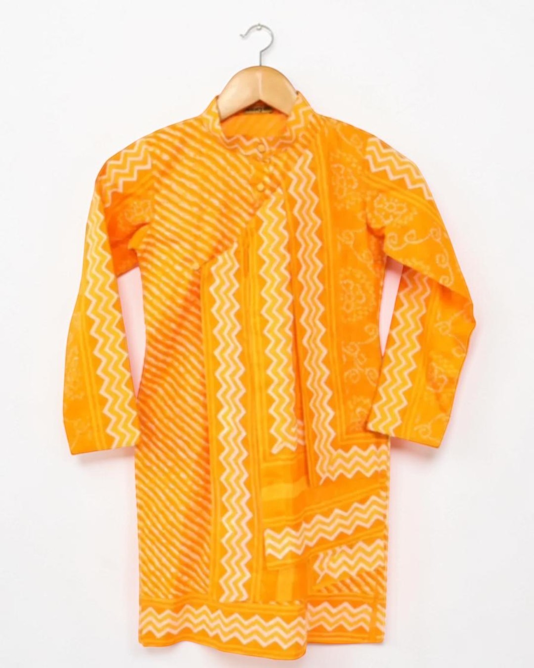 Orange kurta with white patterns on a wooden hanger against a white background
