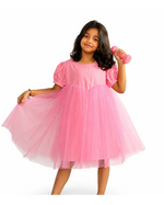 Young girl wearing a pink dress holding a pink toy on a white background