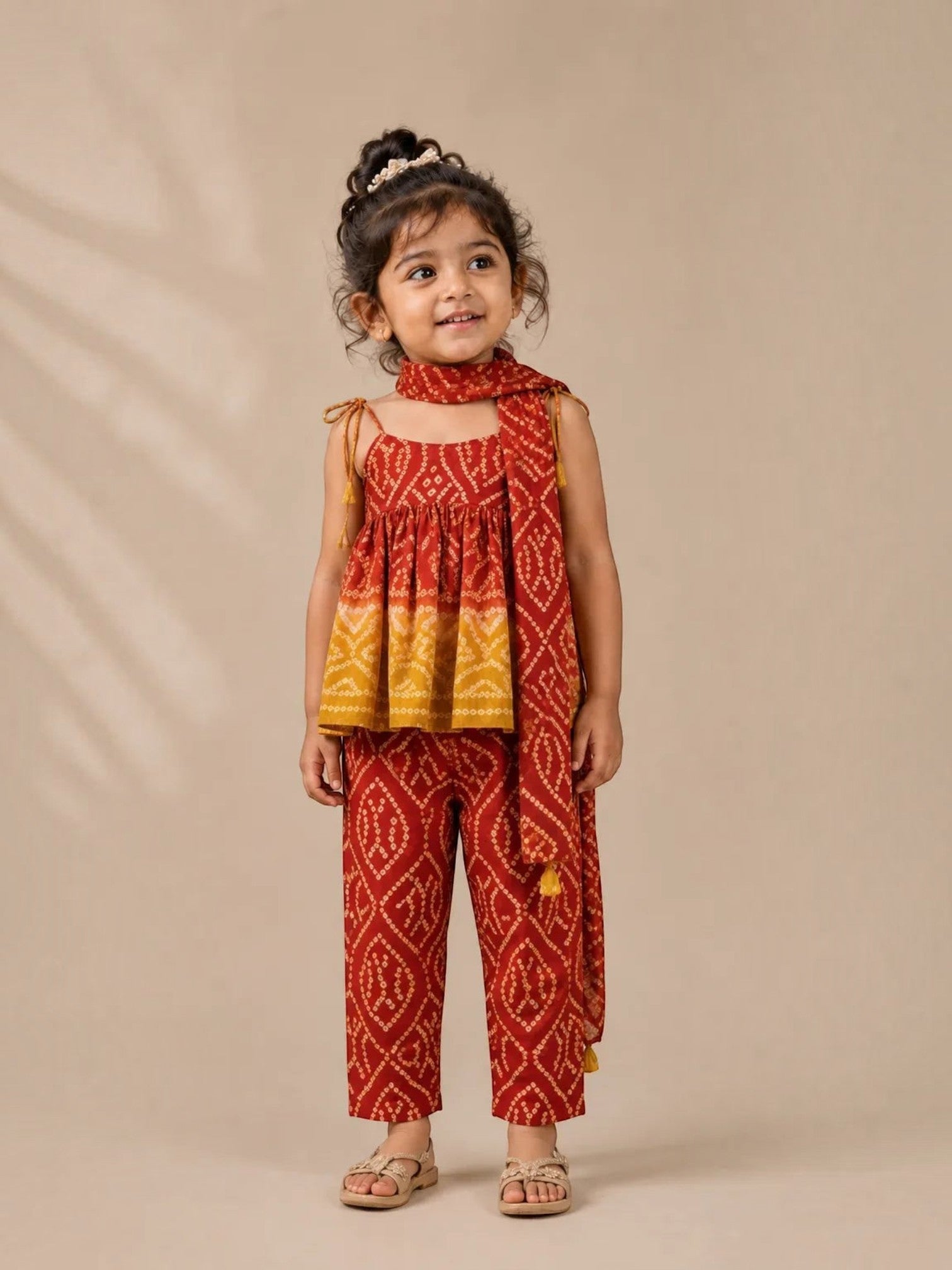 Ameyru Kids Wear girl in a red and yellow bandhani print peplum top, matching trousers, and scarf for festive wear.