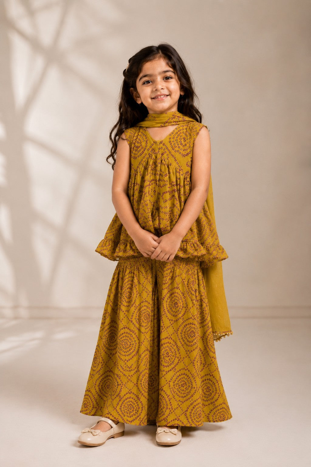 Young girl wearing an Ameyru Kids Wear mustard yellow bandhani print ethnic sharara set with a matching dupatta.