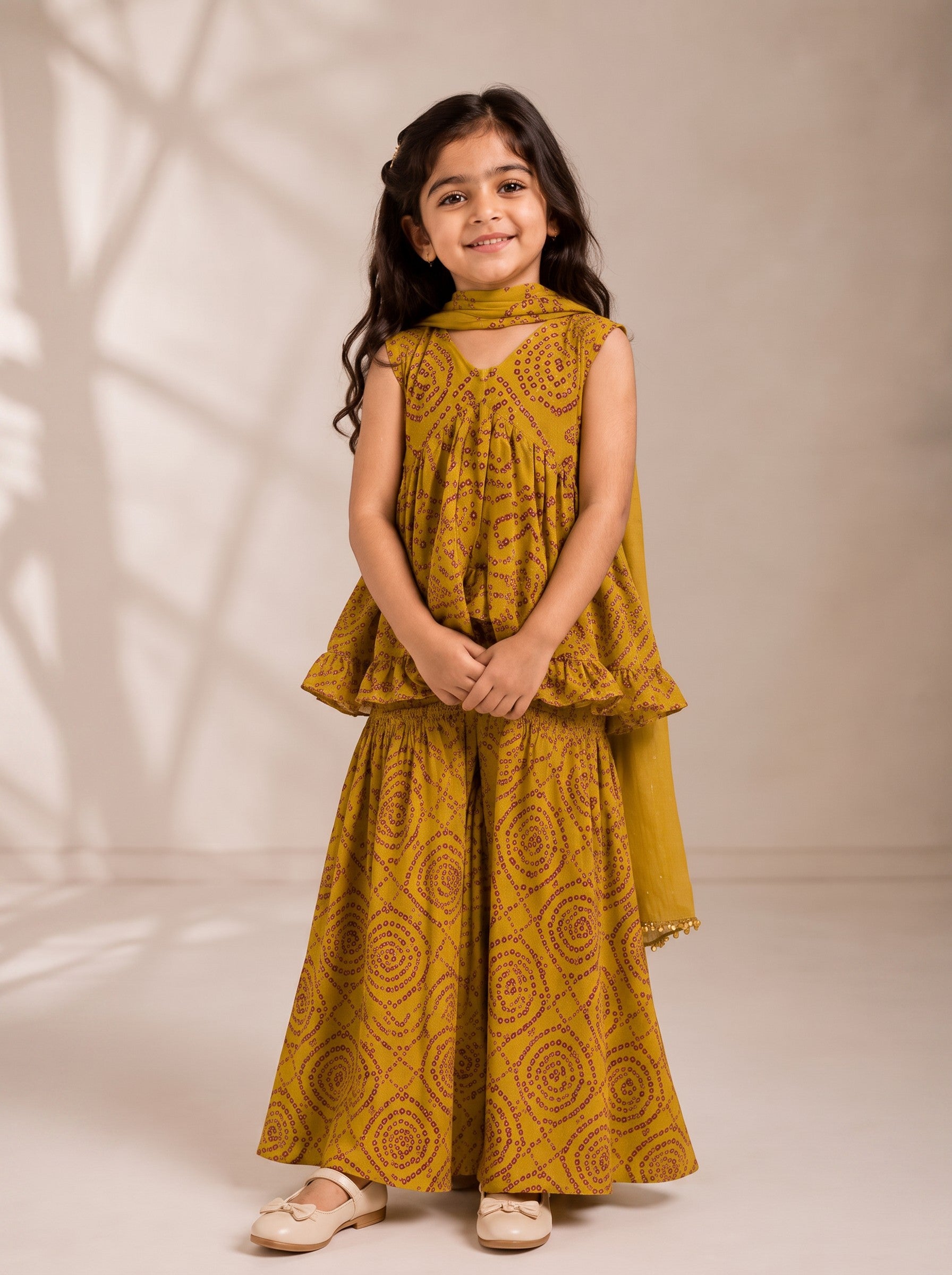 Ameyru Kids Wear mustard yellow bandhani print peplum top and sharara set worn by a smiling young girl.