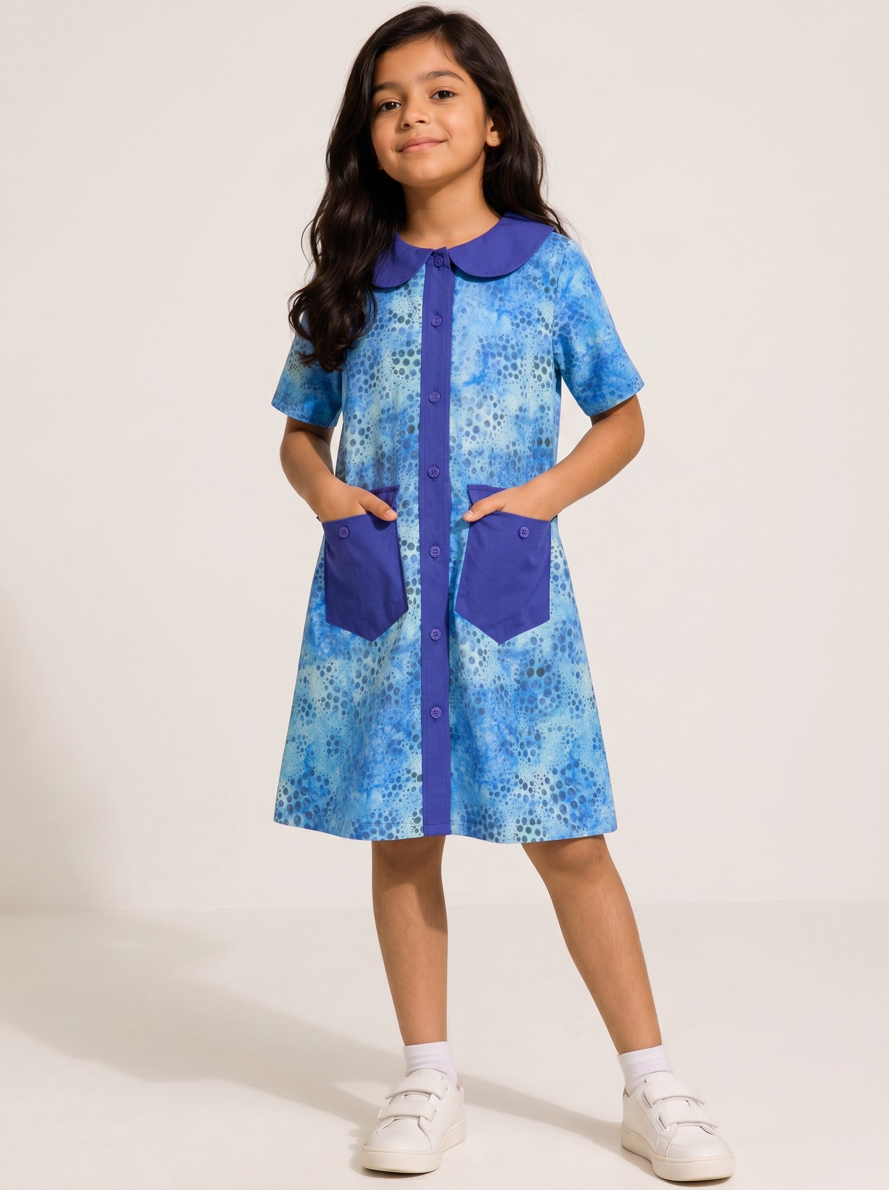 Girl wearing a Baby Kids Cloths blue watercolor dot print A-line dress with a solid collar, button front, and pockets.