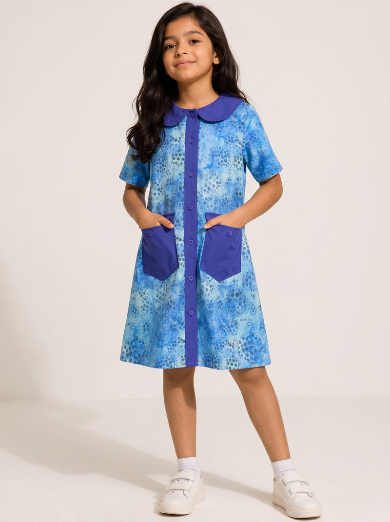 Girl wearing a Baby Kids Cloths blue watercolor dot print A-line dress with a solid collar, button front, and pockets.