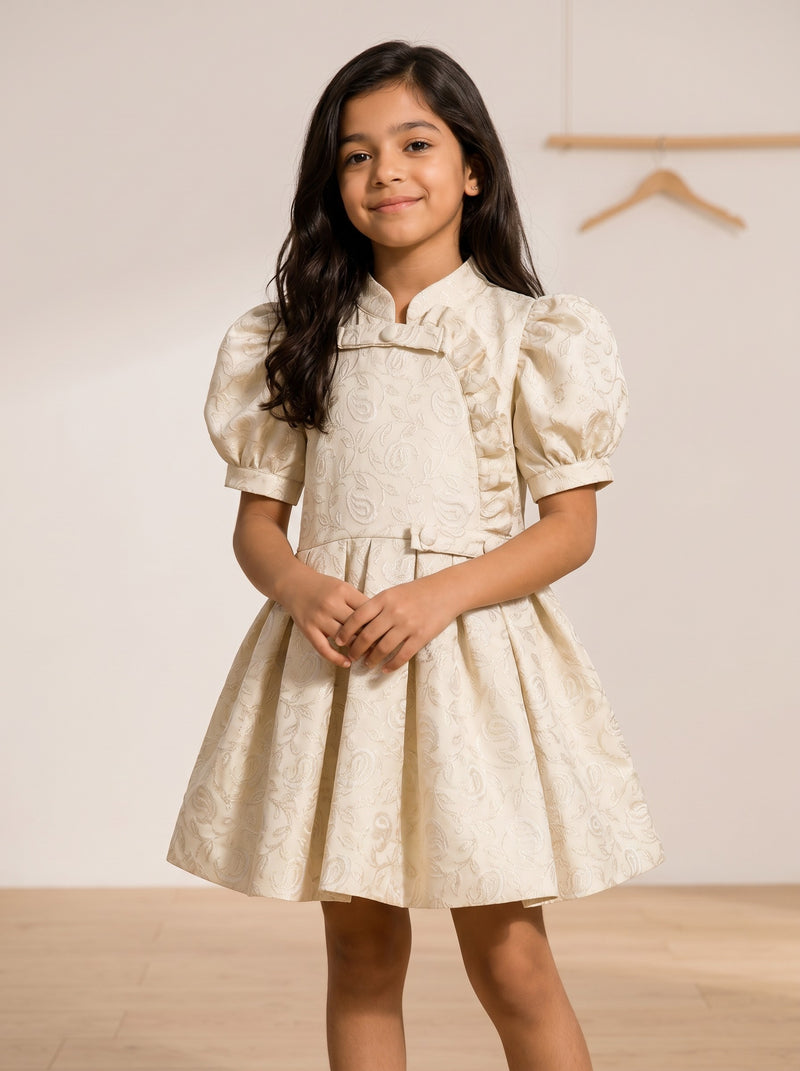 Girl wearing a Baby Kids Cloths cream jacquard dress with puff sleeves, floral pattern, and ruffle side-button detail.